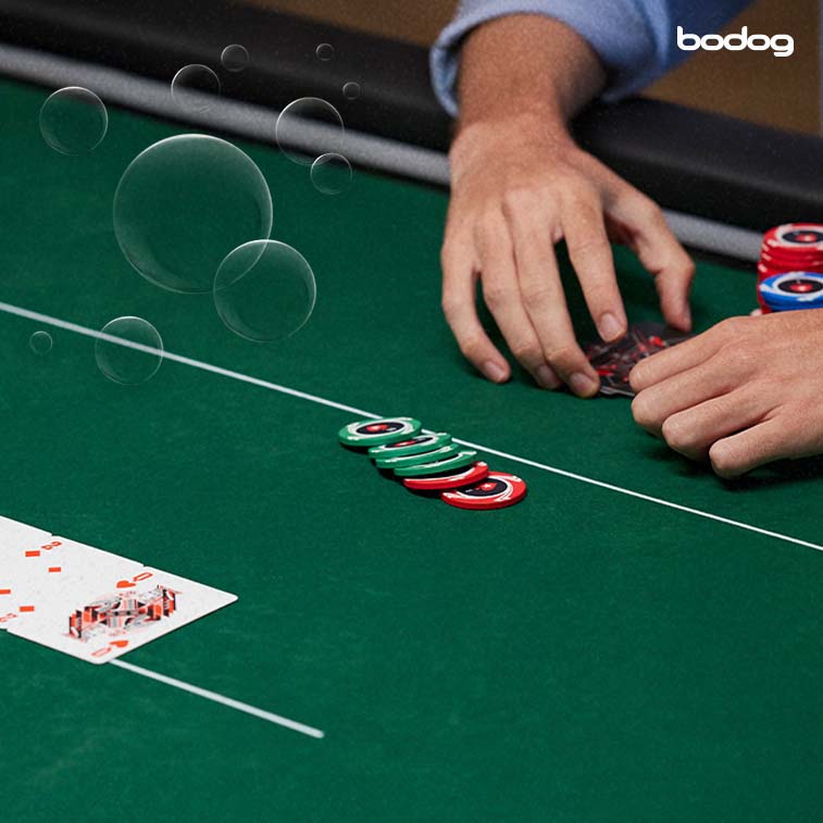 mesa de poker em que se vê duas mãos, fichas, cartas e bolhas artificiais
