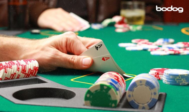 Mão segurando dois ases com fichas de poker ao lado