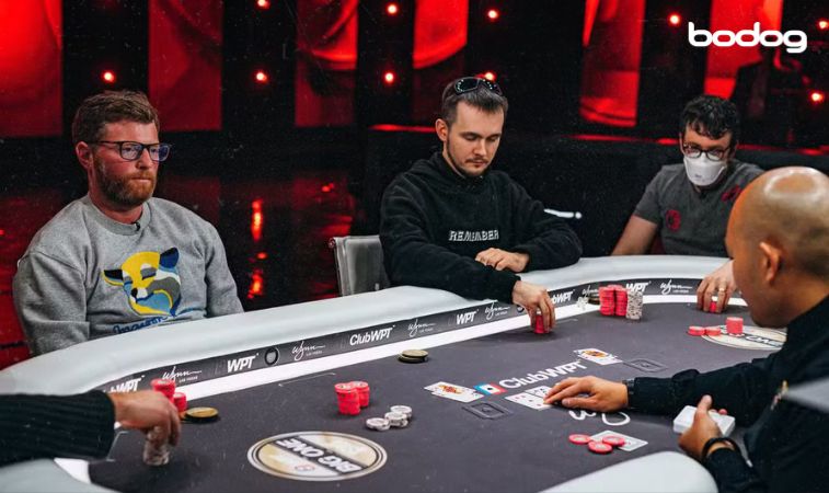 5 homens em uma mesa de poker, 3 deles pegam suas fichas