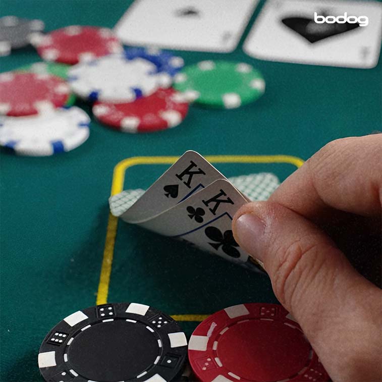 mesa de Baccarat com uma pessoa segurando duas cartas de poker e duas fichas
