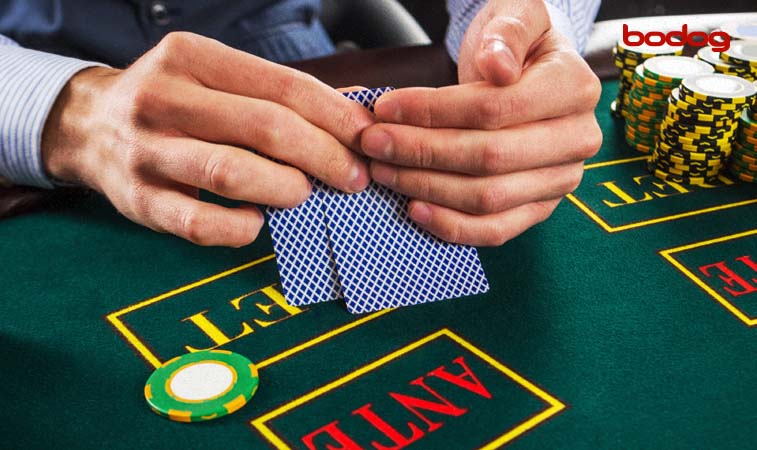 homem segurando duas cartas de baralho em mesa de poker com fichas