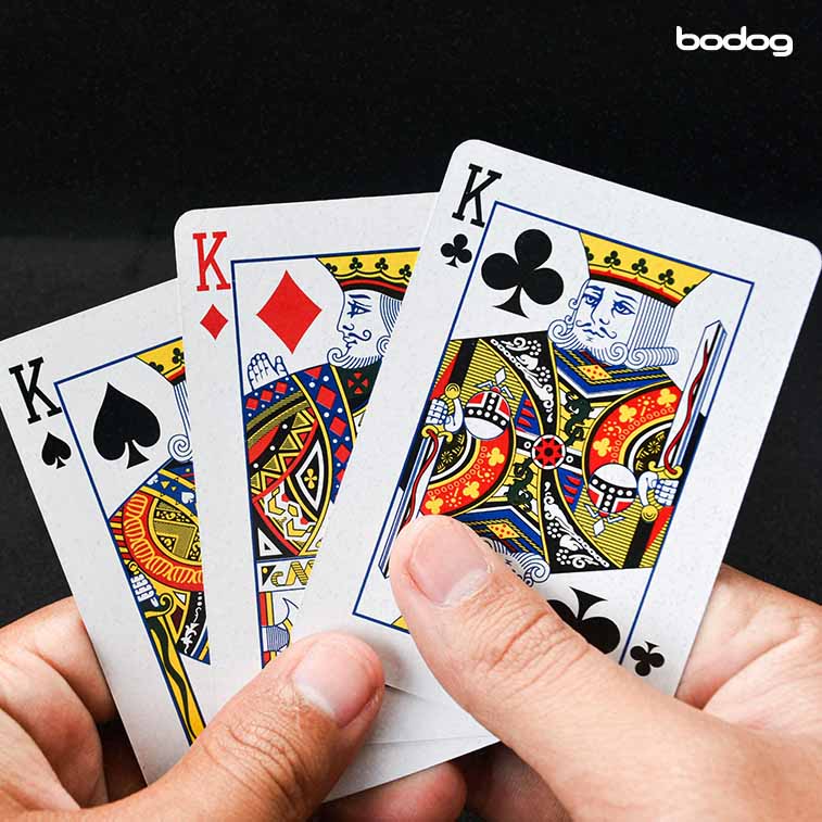pessoa segurando 3 Reis de um baralho de poker