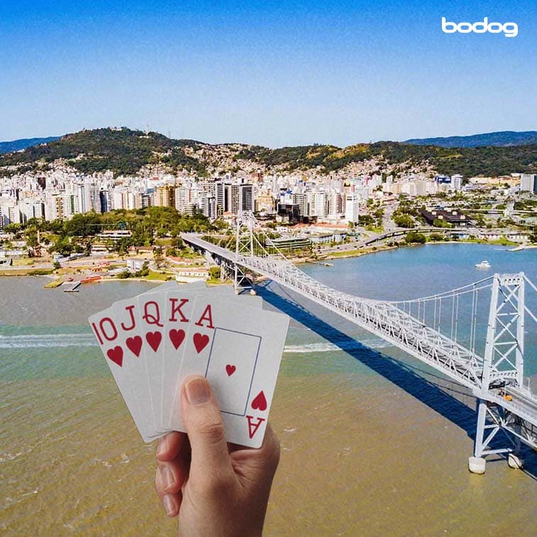 Ponte Hercílio Luz em evidência na imagem com uma mão segurando cartas de poker