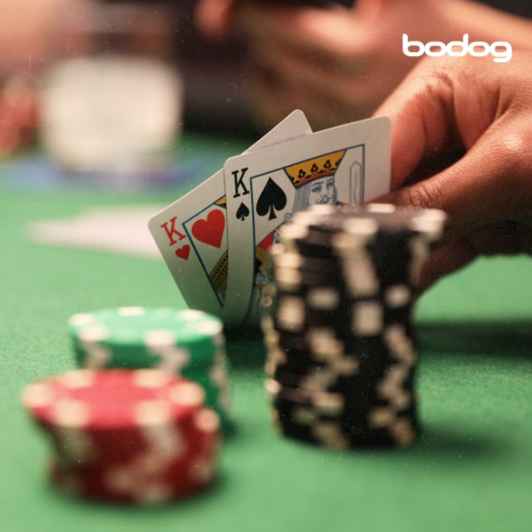Mão com dois reis e fichas de poker sobre uma mesa